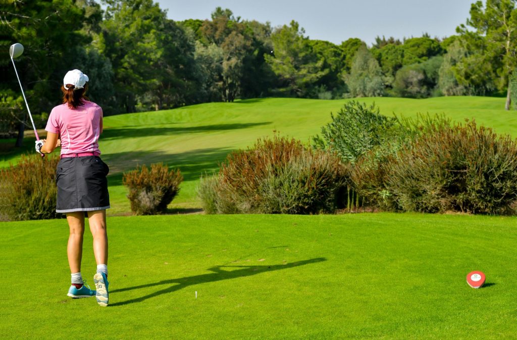 Dos adultos practicando golf en un día soleado en el frondoso campo de golf de Portugal.